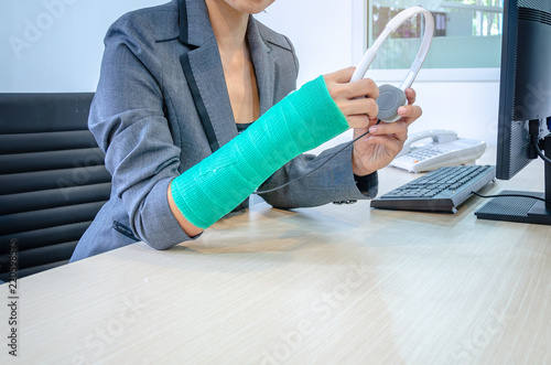 woman with broken hand and green cast  working on computer and holding headphone