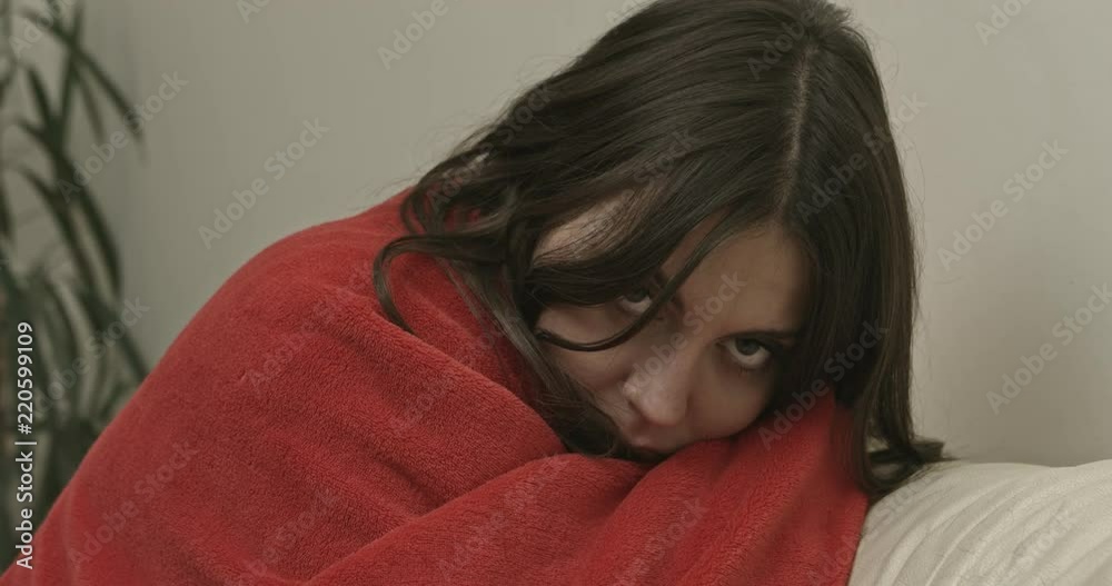 Young woman sitting on sofa covered with blanket Young woman sitting on sofa covered with blanket