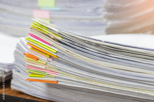 Close up pile of unfinished homework assignment stacked in archive with colorful papers on teacher's table waiting to be managed and inspected. Stack of paperworks. Education and business concept.