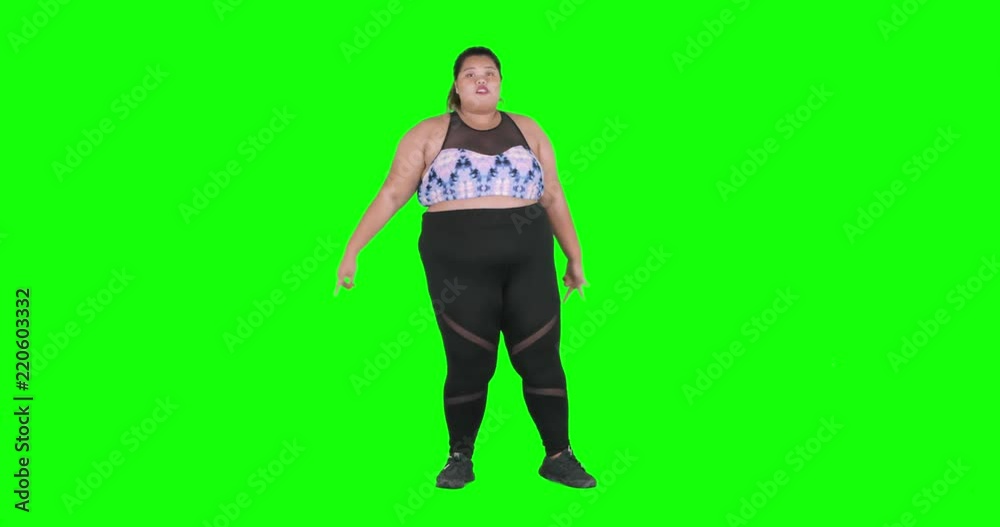 Overweight young woman dancing against green screen background while wearing sportswear in the studio, shot in 4k resolution