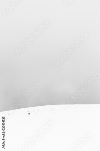 A very minimalistic view of two distant people over a mountain covered by snow, near a fence