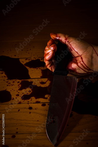 A bloody hand on the floor of a dead suicide victim holding a knife and soaked with blood. For Halloween. 