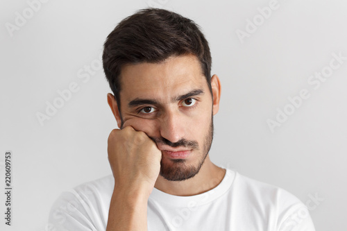 Closeup photo of young caucasian man isolated on gray background dressed casually, pressing hand to chin. looking bored, exhausted and disappointed, feeling helpless and upset, facing problems