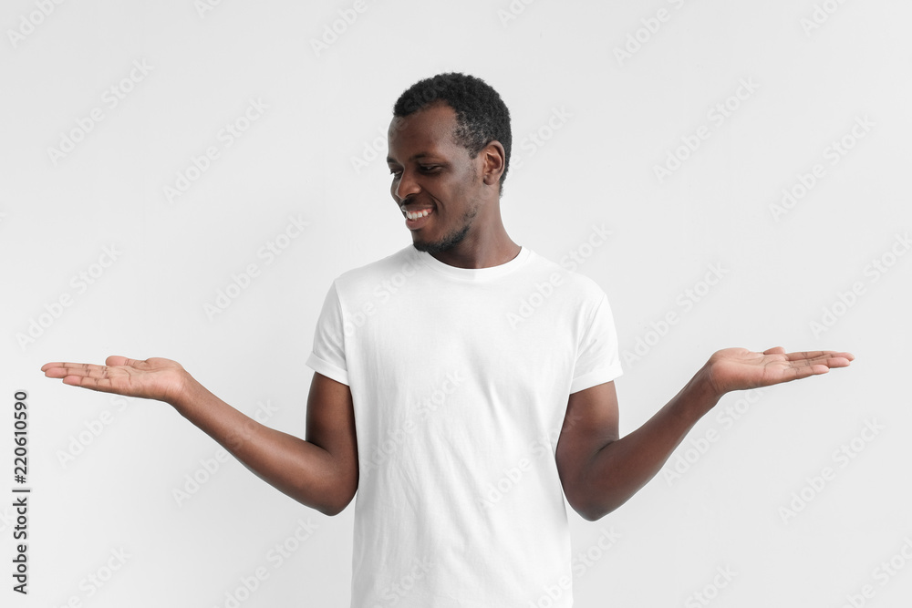 Young african american male choosing between two different options, holding 2 hands, isolated on gray background