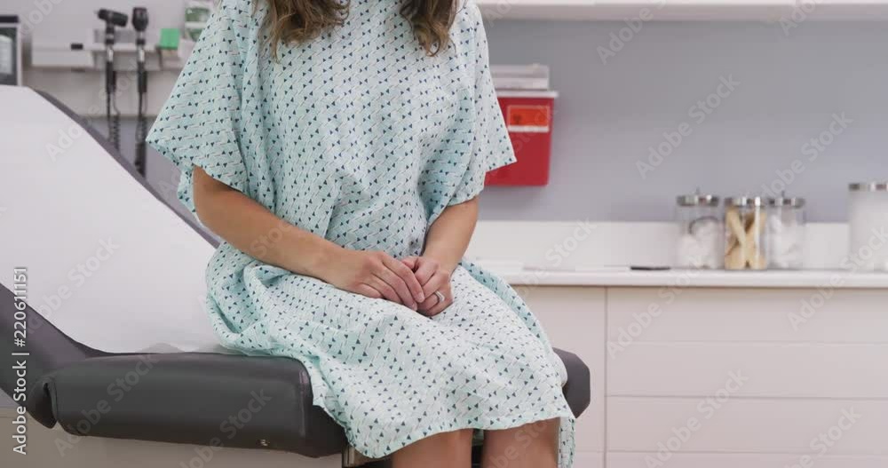 Portrait of young female patient seated on clinic chair wearing hospital gown