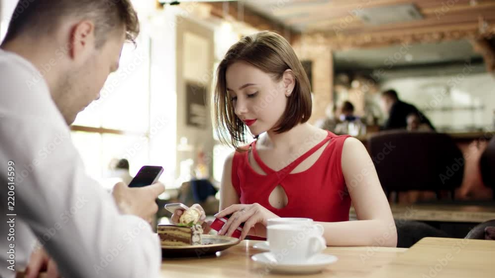 beautiful girl with short hair and in a red dress is sitting in a cafe with her friend with a short brown hairdo in a white shirt and they are talking on the phones beautiful girl with short hair and in a red dress is sitting in a cafe with her friend with a short brown hairdo in a white shirt and they are talking on the phones