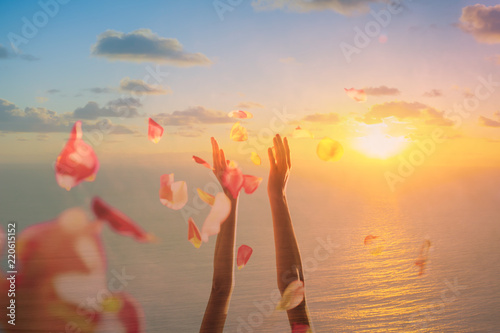 Celebration, happiness, joy concept. Hand throwing rose pedals in the air against a beautiful sunset. Double exposure.