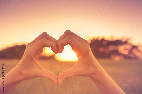 Hand shaped heart against beautiful sunset.