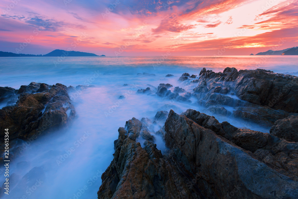 Long exposure image of Dramatic sky and wave seascape with rock in sunset scenery background.