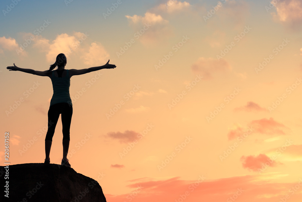 Happiness and freedom.Young woman on a mountain with arms up enjoying the beautiful sunset. 
