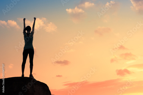 Strong motivate woman standing on rock with fist in the air.