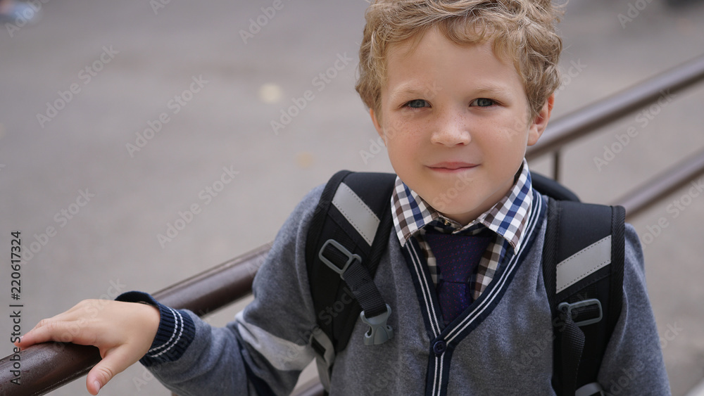 Little Caucasian curly boy in school uniform with backpack comes up on stairs. Little Caucasian curly boy in school uniform with backpack comes up on stairs.