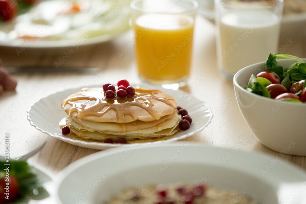 Close up of tasty fluffy pancakes topped with syrup with berries aside served on kitchen table, delicious homemade breakfast dishes prepared on tabletop, appetizing morning food and drinks Close up of tasty fluffy pancakes topped with syrup with berries aside served on kitchen table, delicious homemade breakfast dishes prepared on tabletop, appetizing morning food and drinks