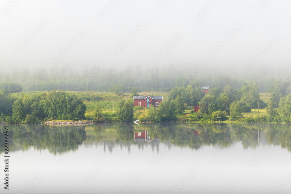 Old farm at a mirrored lake with morning mist