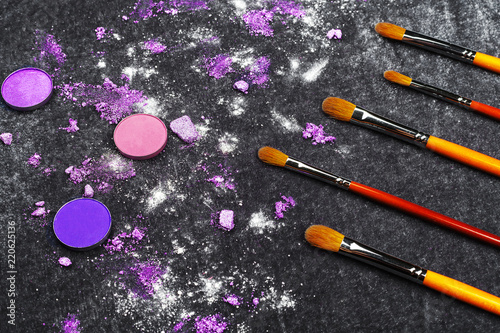 professional brushes and purple crashed eye shadows lying on a black background. concept of healthy cosmetics. free space for text photo