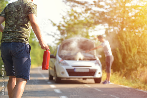 Brave man with fire extinguisher going to a car incident on the road with smoke on the engine