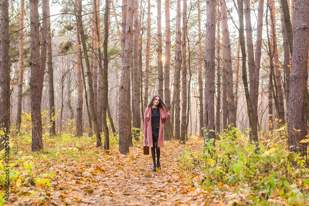 Autumn, fashion, people concept - woman with brown retro suitcase walking through the autumn park and smiling