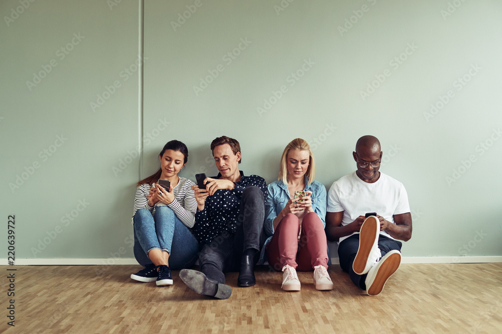 Diverse coworkers sitting on an office floor using their cellpho