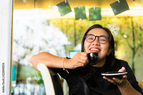 Happy asian woman with eye glasses smiling  and drinking coffee in cafe photo