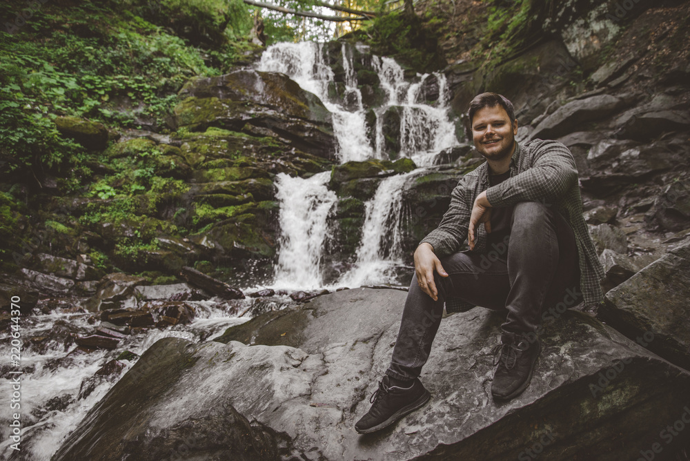 man sitting at rock with waterfall on background