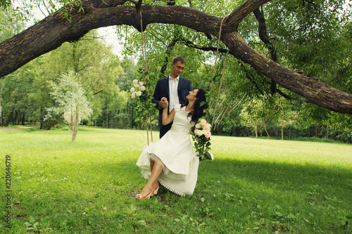 Beautiful swings are suspended in the park on a tree and newlyweds are sitting on them