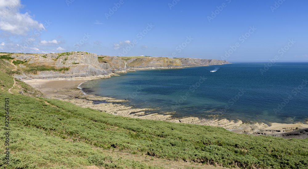 A sweeping bay, on the South Wales coast, as viewed from the Wales Coastal Path. The day is sunny and the water is blue.