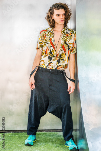 Hispanic American Artist with brown curly hair in New York, wearing colorful patterned short sleeve shirt, baggy loose pants with suspenders, patterned sneakers, hanging old key as necklace.