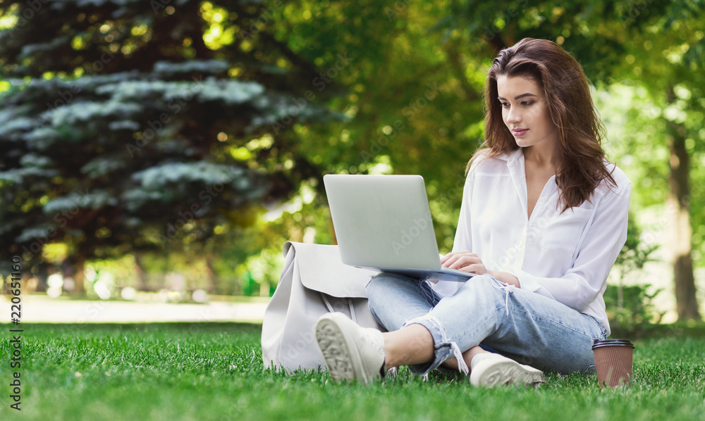 Pretty woman sitting in park and using laptop Pretty woman sitting in park and using laptop