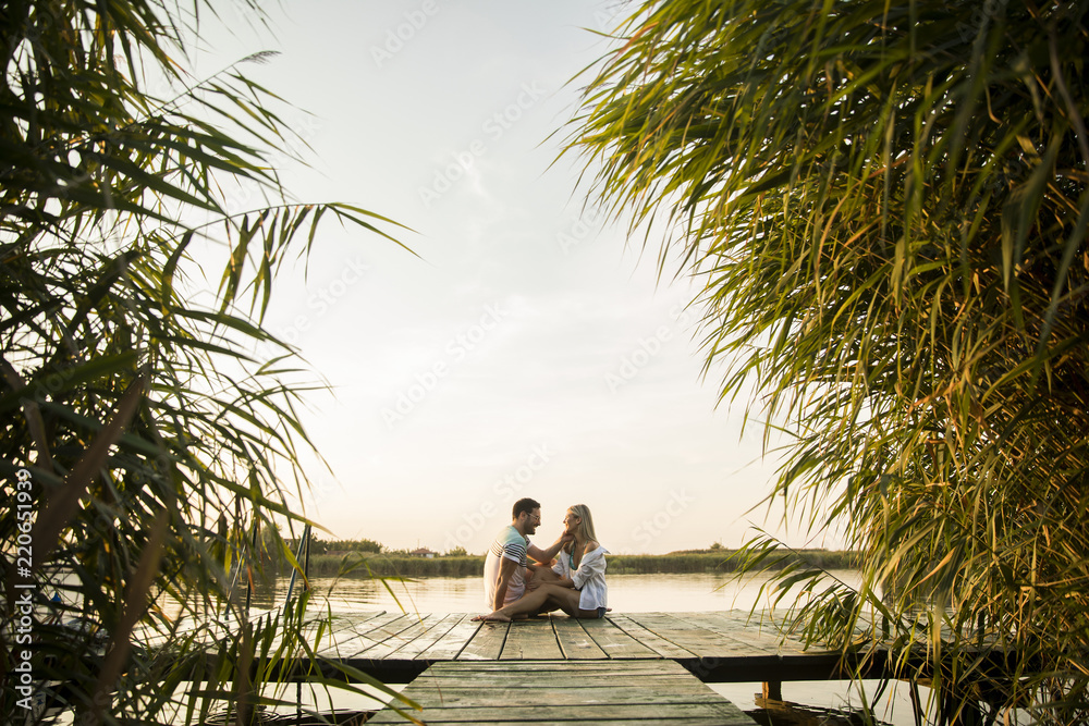 Romantic couple sitting on the wooden pier on the lake