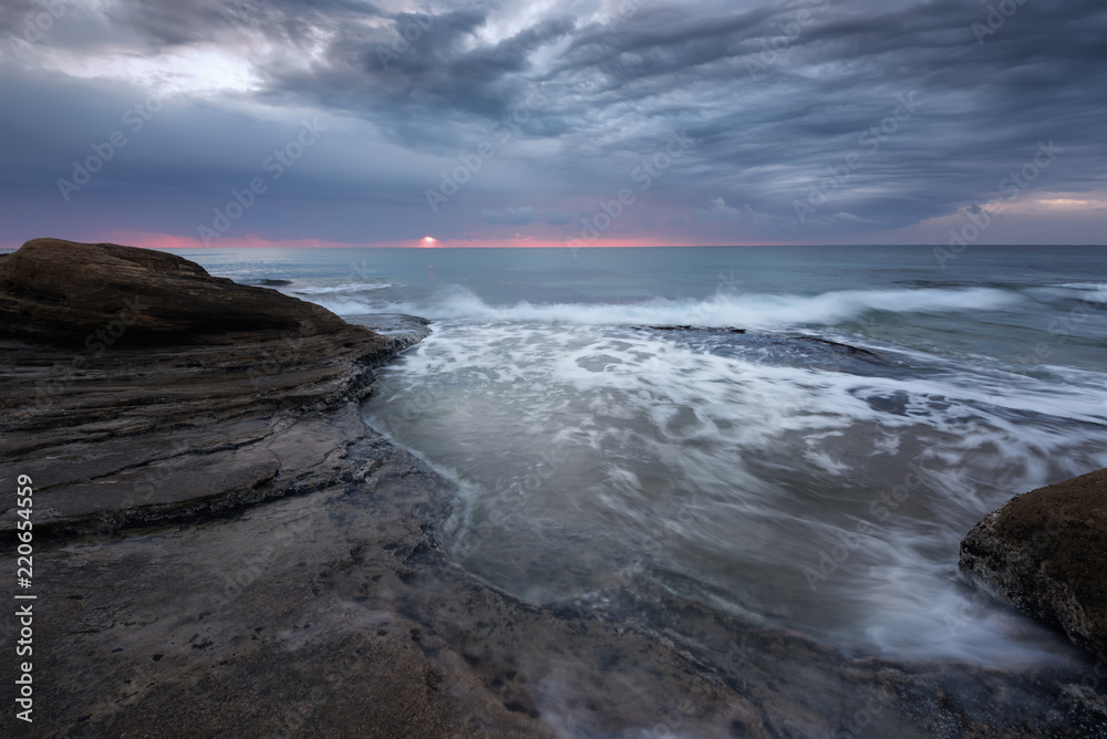 Obraz premium Seascape during sunrise. Beautiful natural seascape, blue hour. Sea sunrise at the Black Sea coast. Magnificent sunrise with clouds and fire sun in the middle of December.Ravda, Bulgaria