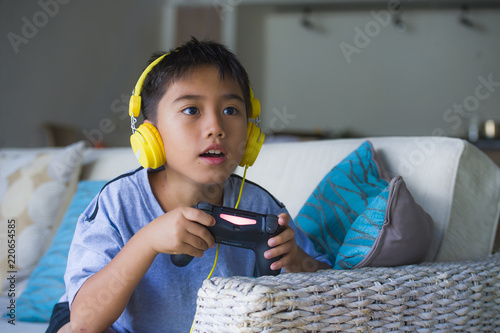 young Latin little child excited and happy playing video game online with headphones holding controller having fun sitting on couch in kid gaming addiction photo