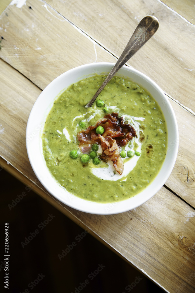 Overhead shot of creamy green pea soup with fried bacon and herbs on rustic wooden background Overhead shot of creamy green pea soup with fried bacon and herbs on rustic wooden background