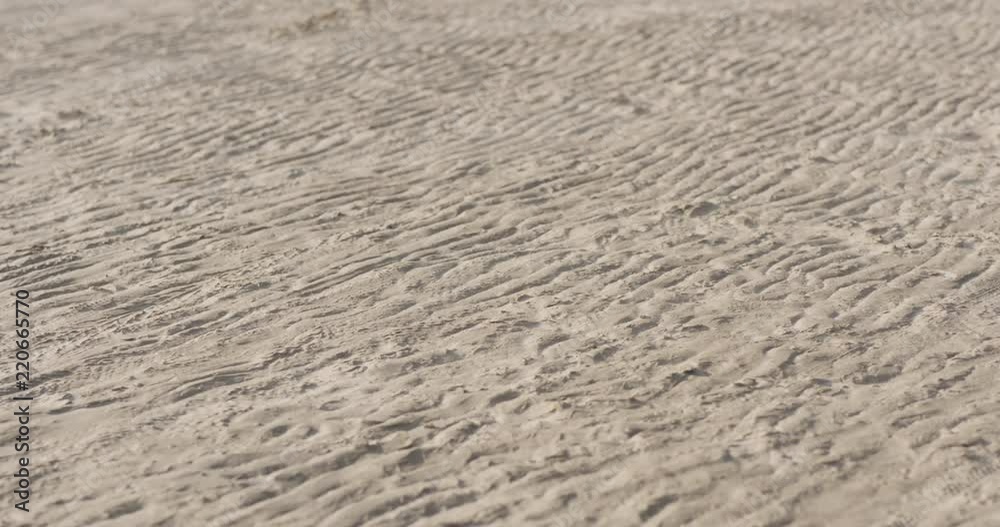Slow motion wind blows sand on a beach at midday Slow motion wind blows sand on a beach at midday