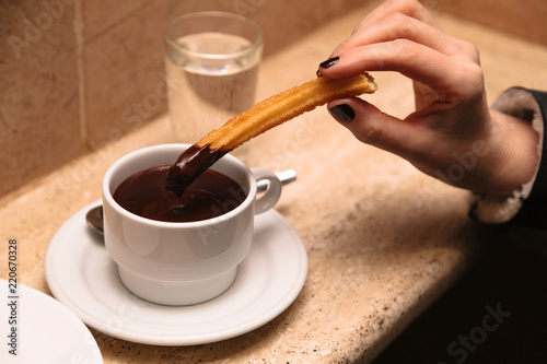 Cup with hot chocolate and hand of girl holding churros