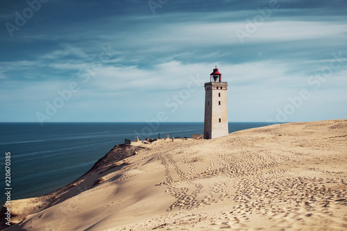 Fototapeta Naklejka Na Ścianę i Meble -  Bright beach sand dunes with the famous danish landmark lighthouse with blue sky background. Rubjerg Knude Lighthouse, Lønstrup in North Jutland in Denmark, Skagerrak, North Sea