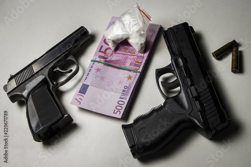 Black gun with a pack of euros and packets of drugs on a white table