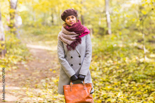 Autumn, nature, people concept - beautiful young woman in a grey coat and a beret standing in the park. © satura_