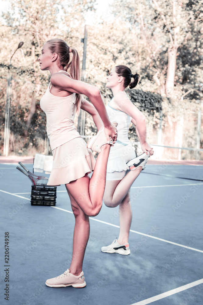 Quad stretch. Cheerful two women stretching on court and staying in profile