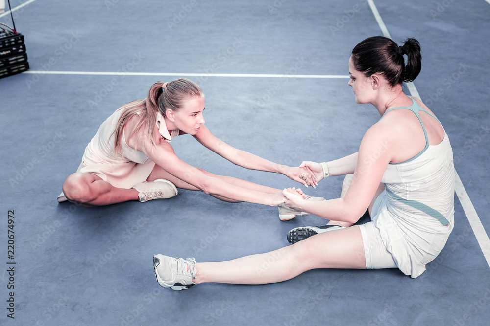 Obraz premium Team stretching. Positive two women stretching on court and communicating