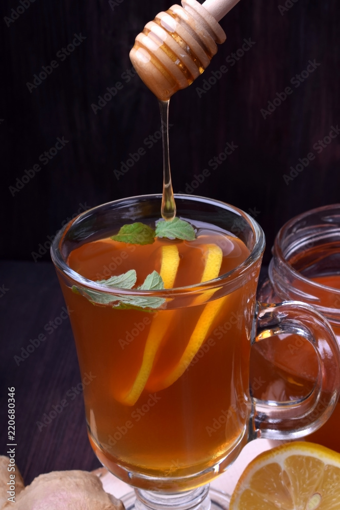 Tea with lemon and mint in a glass. Honey is dripping from the wooden spoon Tea with lemon and mint in a glass. Honey is dripping from the wooden spoon