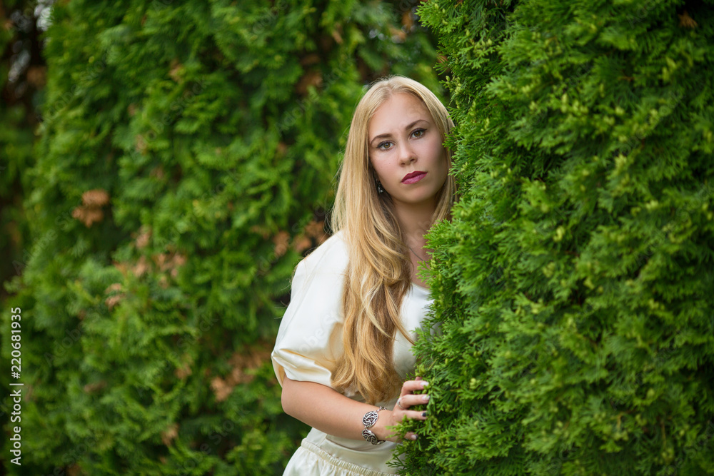 Portrait of a young pretty blonde girl in a dress between thuja on the street in autumn. Portrait of a young pretty blonde girl in a dress between thuja on the street in autumn.