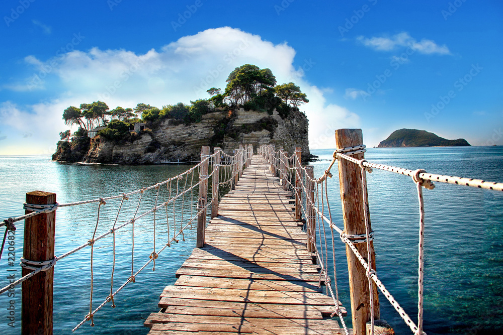 Fototapeta premium Drewniany most z widokiem na morze prowadzi na wyspę z palmami. To most linowy. Znajduje się w Zakynthos w Grecji.