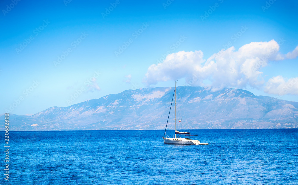 The yacht sails along the clear waters of the Mediterranean Sea off the island of Zakynthos. The neighboring island of Kefalonia can be seen from here. There is a beautiful blue sky with several cloud