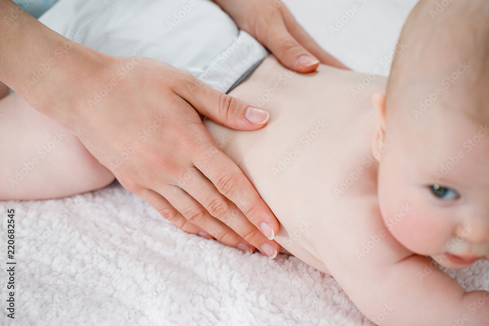 Mother's hands massage the muscles of the back of her baby. Preventive gymnastics. Light background Mother's hands massage the muscles of the back of her baby. Preventive gymnastics. Light background