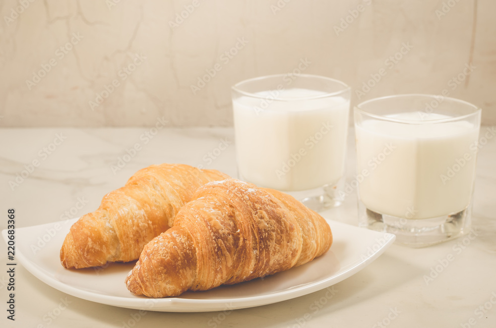 breakfast with croissants and milk/croissants in a white plate and two glasses milk on a marble background. Selective focus breakfast with croissants and milk/croissants in a white plate and two glasses milk on a marble background. Selective focus