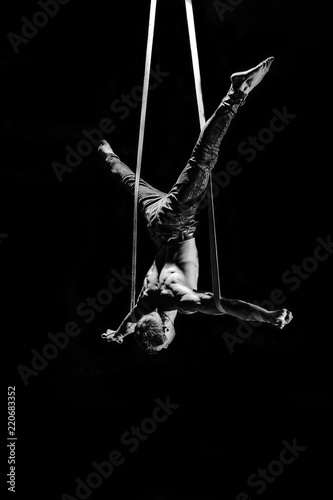 Canvas Print Circus artist on the aerial straps making cross with strong muscles on black bac