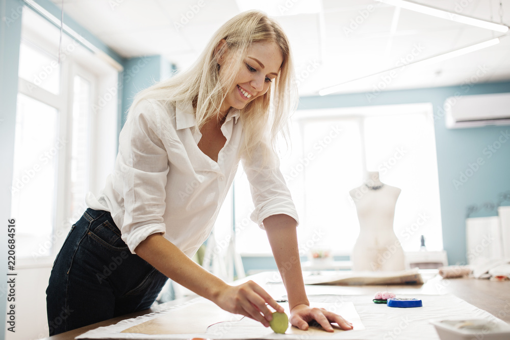 A smart-looking blond woman is lining a sewing cutting-out with a piece of soap. Fasion, tailor's workshop. A smart-looking blond woman is lining a sewing cutting-out with a piece of soap. Fasion, tailor's workshop.