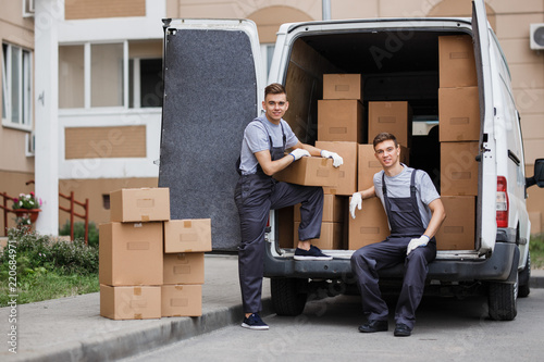 Fotografía Two young handsome smiling movers wearing uniforms are unloading the van full of boxes