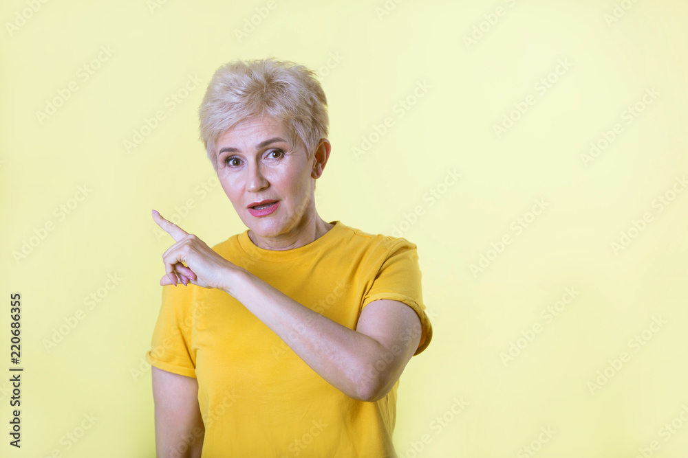 beautiful stylish woman with a short hairstyle on a yellow background pointing with her finger