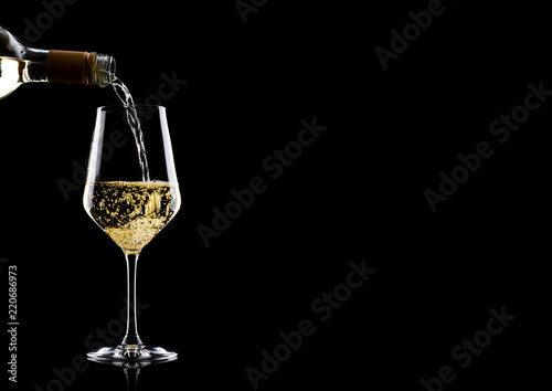 Pouring white wine from bottle to glass on black with space for your text